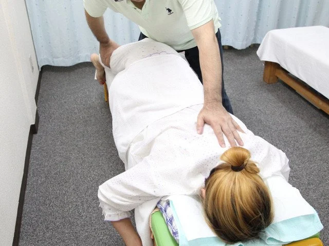 옆으로 누운 상태에서 허리 주변의 가동 범위를 확인하며 수기요법을 시행하는 시술자의 손 부분